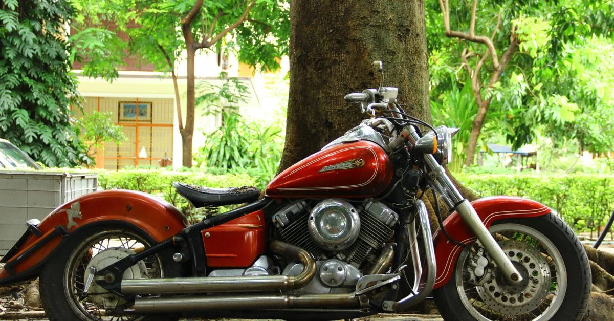 Une moto rouge classique est garée près d'un arbre dans un cadre extérieur, mettant en valeur le charme vintage.