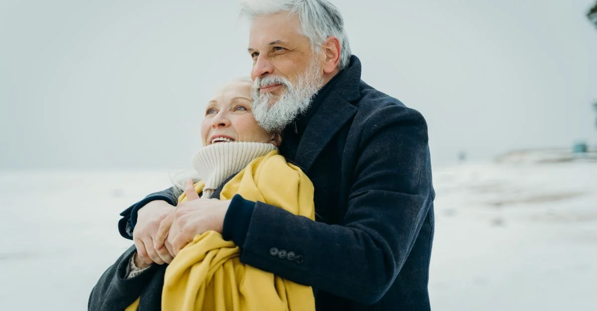 Couple âgé s'embrassant chaleureusement sur une plage enneigée. Amour et connexion en hiver.