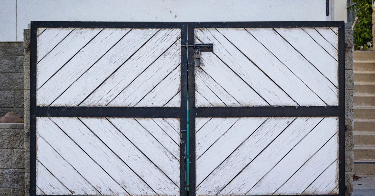 Un portail en bois blanc rustique avec des panneaux diagonaux et un cadre en métal noir à l'entrée d'une résidence.