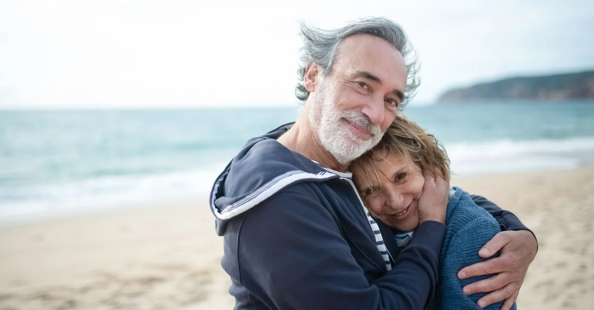 Un couple âgé joyeux s'embrasse sur une plage sereine au Portugal, capturant l'amour et le bonheur.