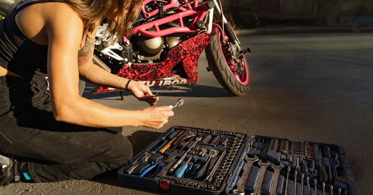 Une femme répare une moto avec un ensemble d'outils complet en plein air pendant la journée.